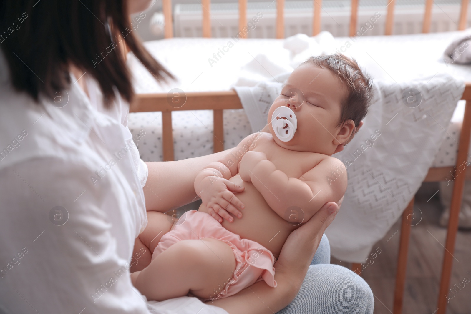 Photo of Mother holding her cute little baby with pacifier at home, closeup