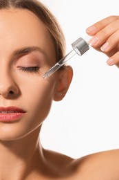 Woman applying cosmetic serum onto her face on white background, closeup