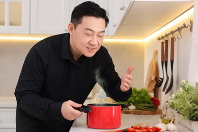 Photo of Man smelling dish after cooking at countertop in kitchen