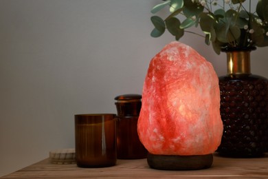 Beautiful Himalayan salt lamp, eucalyptus branches and candles on wooden table indoors, space for text