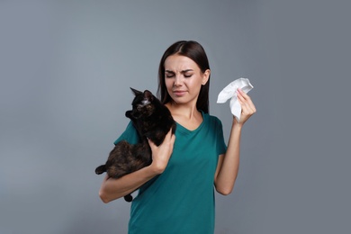 Photo of Young woman with cat suffering from allergy on grey background