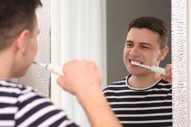 Man brushing his teeth with electric toothbrush near mirror in bathroom