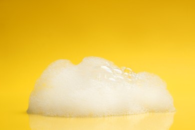 Photo of Drop of fluffy bath foam on yellow background