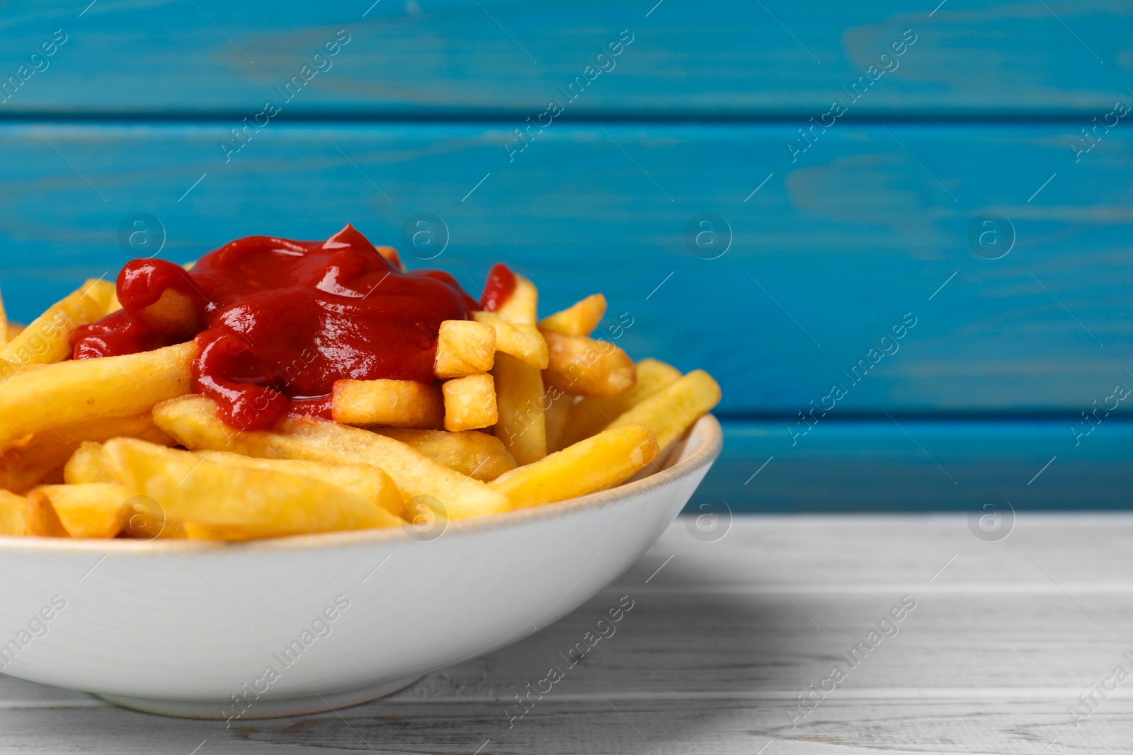 Photo of Bowl of tasty french fries on white wooden table, space for text