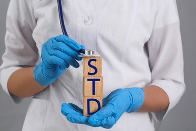 Doctor holding wooden cubes with abbreviation STD and stethoscope on grey background, closeup