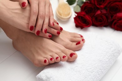 Photo of Woman showing stylish toenails after pedicure procedure and manicured hands with red polish on white wooden floor, closeup
