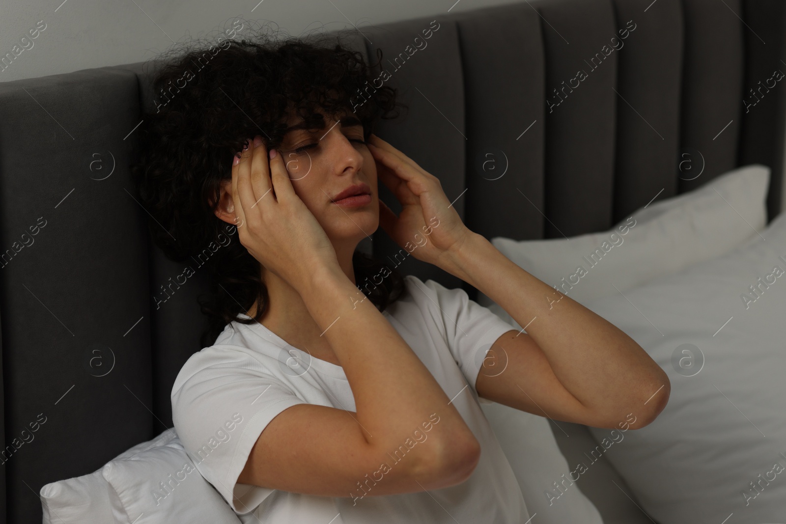 Photo of Young woman suffering from headache in bed at night