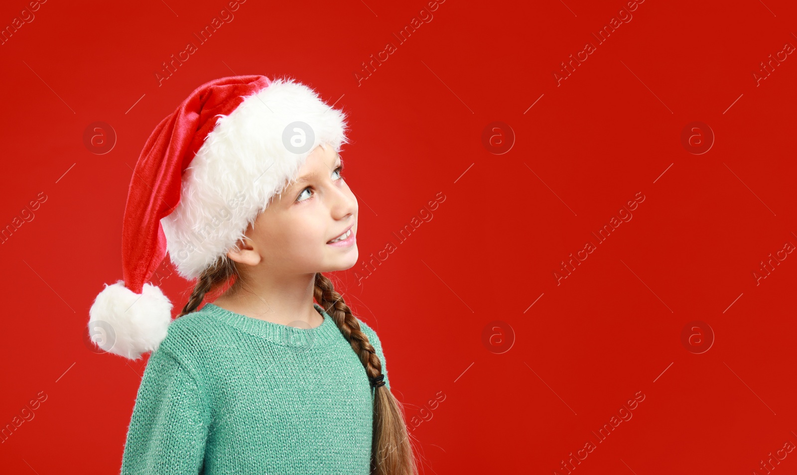 Image of Happy little child in Santa hat on red background, space for text. Christmas celebration