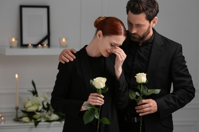 Photo of Sad couple with white roses mourning indoors. Funeral ceremony
