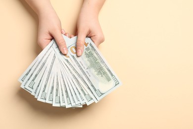 Money exchange. Woman holding dollar banknotes on beige background, top view. Space for text