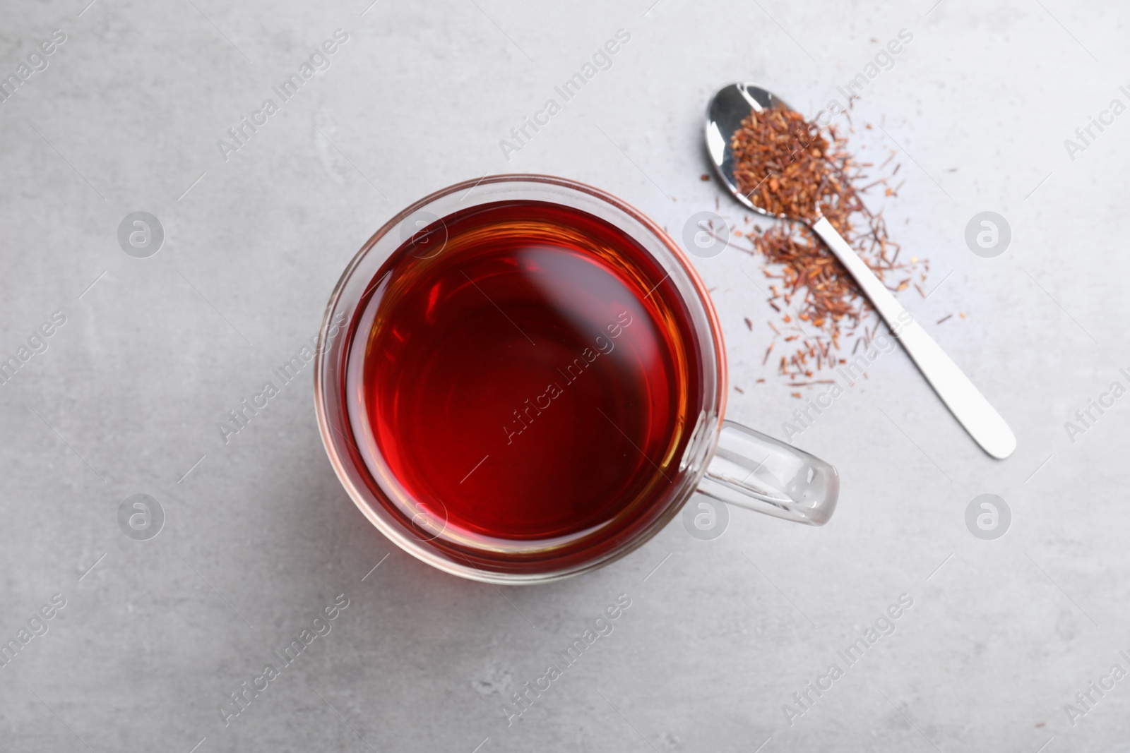 Photo of Freshly brewed rooibos tea, scattered dry leaves and spoon on grey table, flat lay