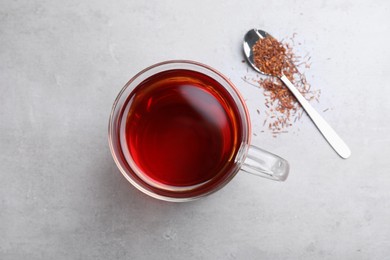 Photo of Freshly brewed rooibos tea, scattered dry leaves and spoon on grey table, flat lay
