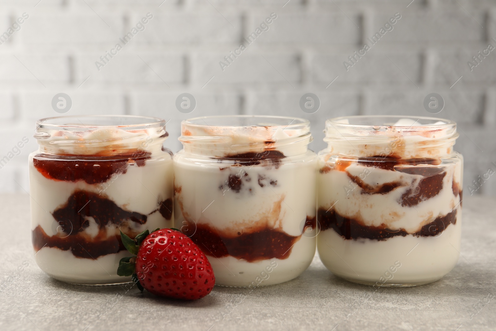 Photo of Tasty yoghurt with jam and strawberry on grey table, closeup