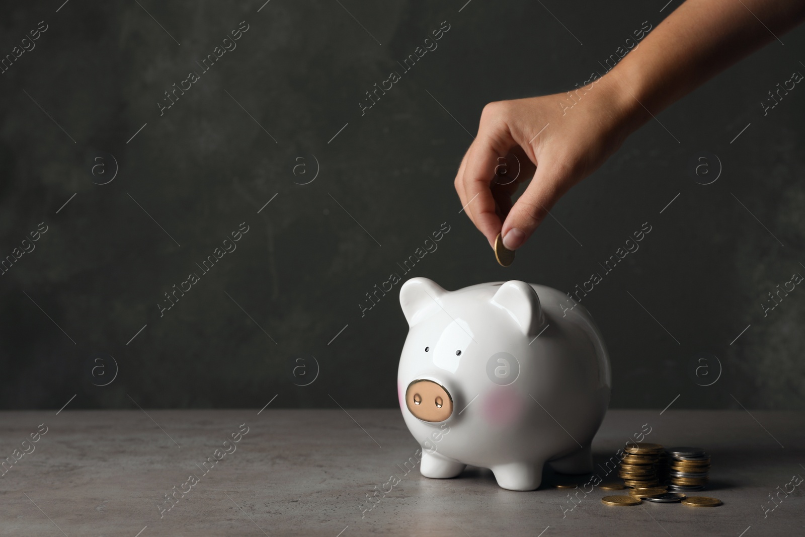 Photo of Woman putting coin into piggy bank on table. Space for text