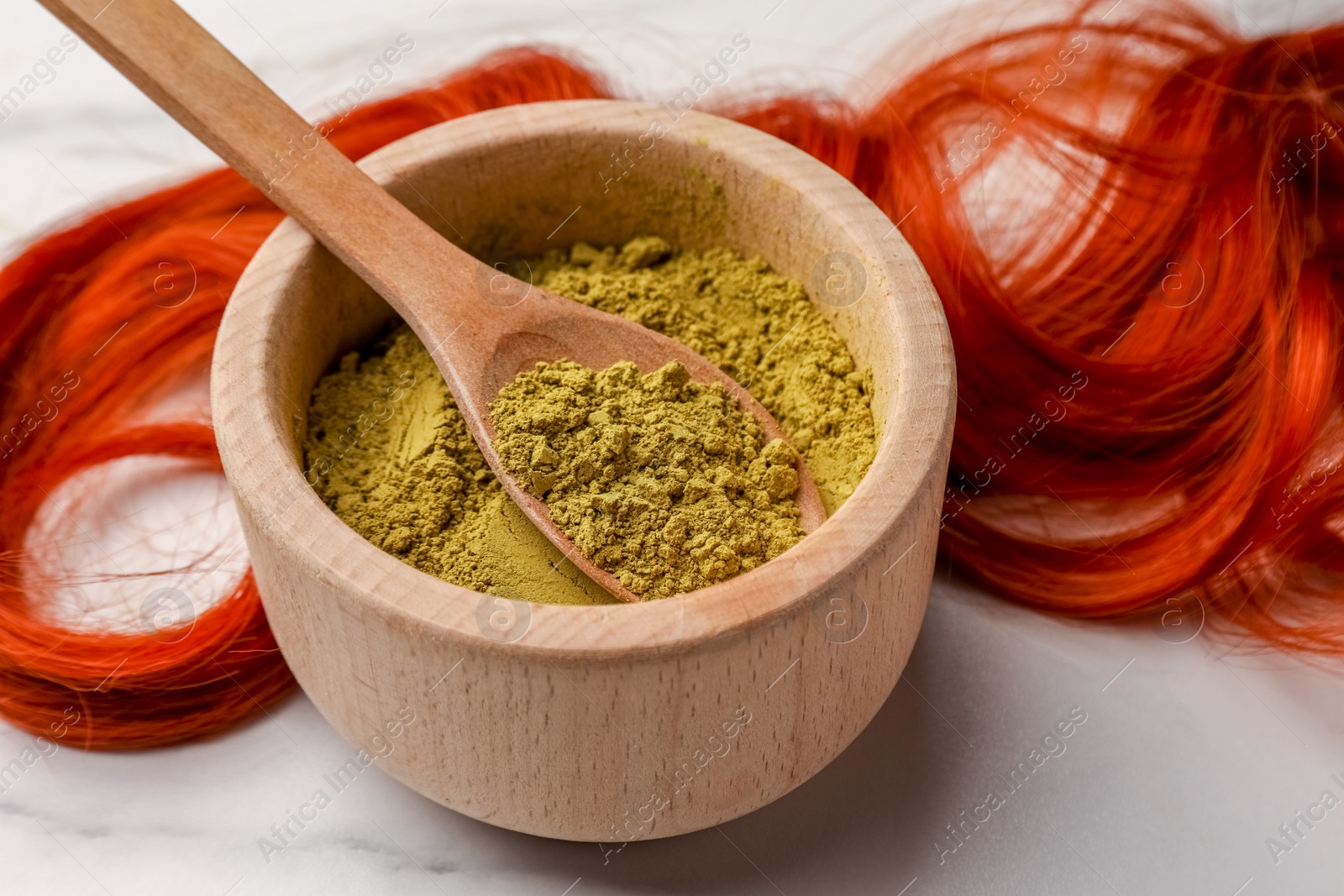 Photo of Bowl of henna powder and red strand on white marble table, closeup. Natural hair coloring