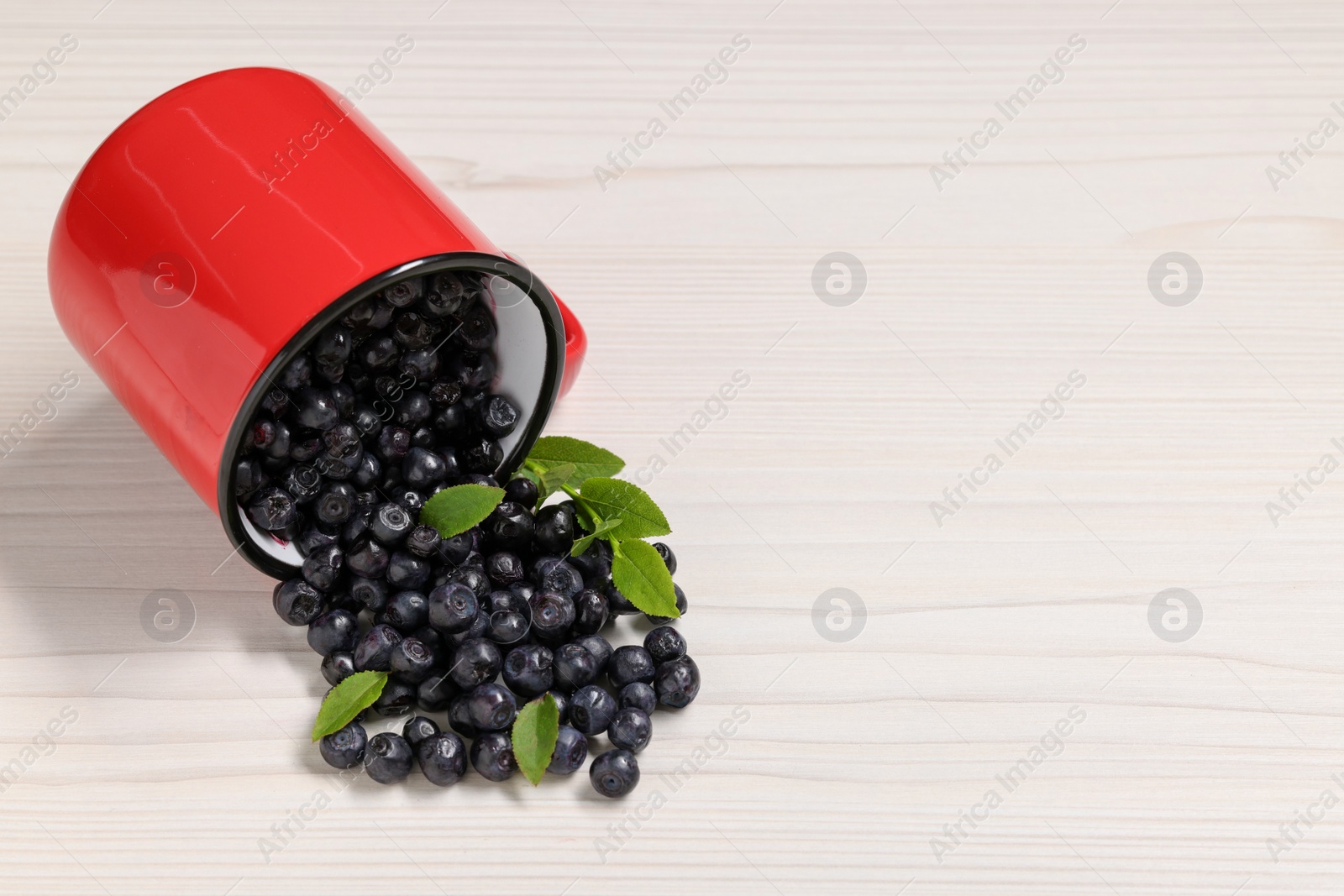 Photo of Mug with ripe bilberries on white wooden table. Space for text