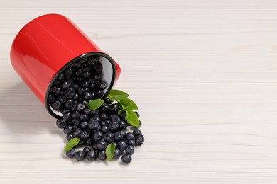 Mug with ripe bilberries on white wooden table. Space for text