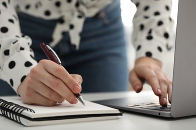 E-learning. Woman taking notes during online lesson at table indoors, closeup