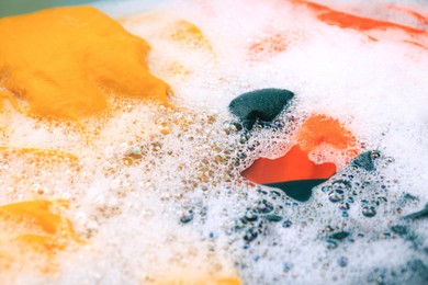 Photo of Colorful clothes in suds, closeup. Hand washing laundry