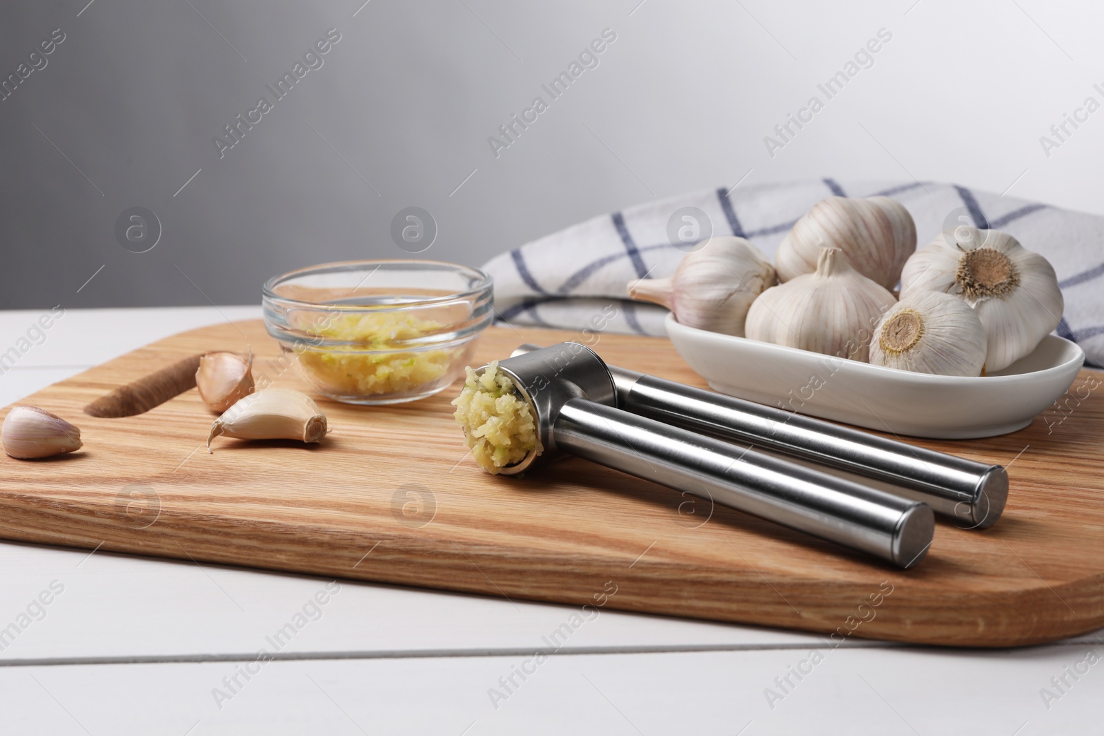 Photo of One metal press and garlic on white wooden table