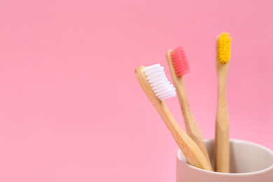 Toothbrushes made of bamboo in holder on pink background. Space for text