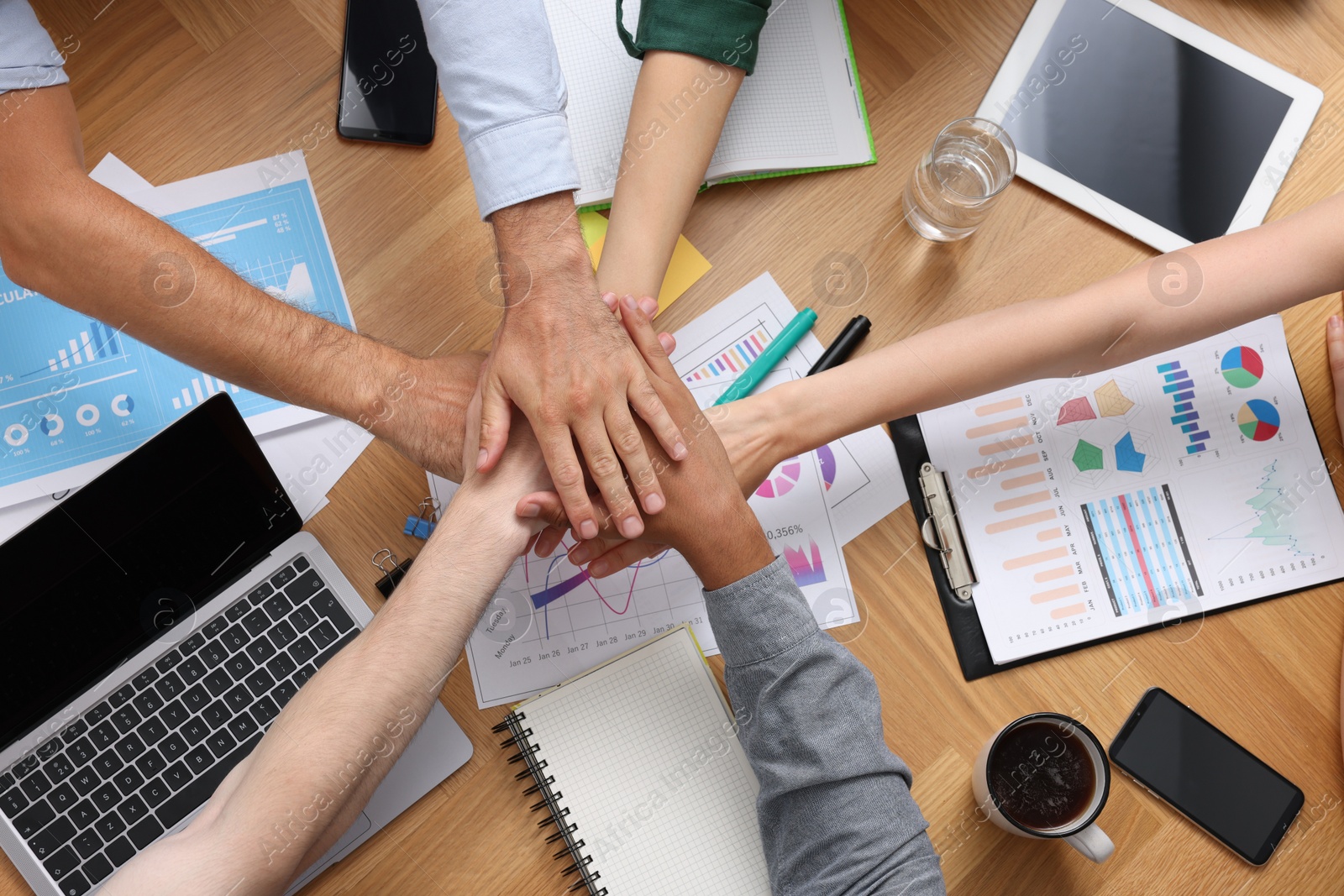 Photo of Team of employees putting hands together at wooden table, top view. Startup project