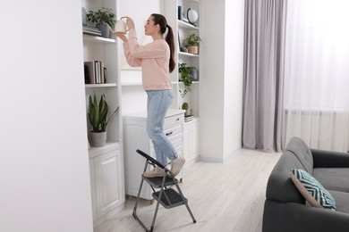 Photo of Woman on ladder watering houseplant at home