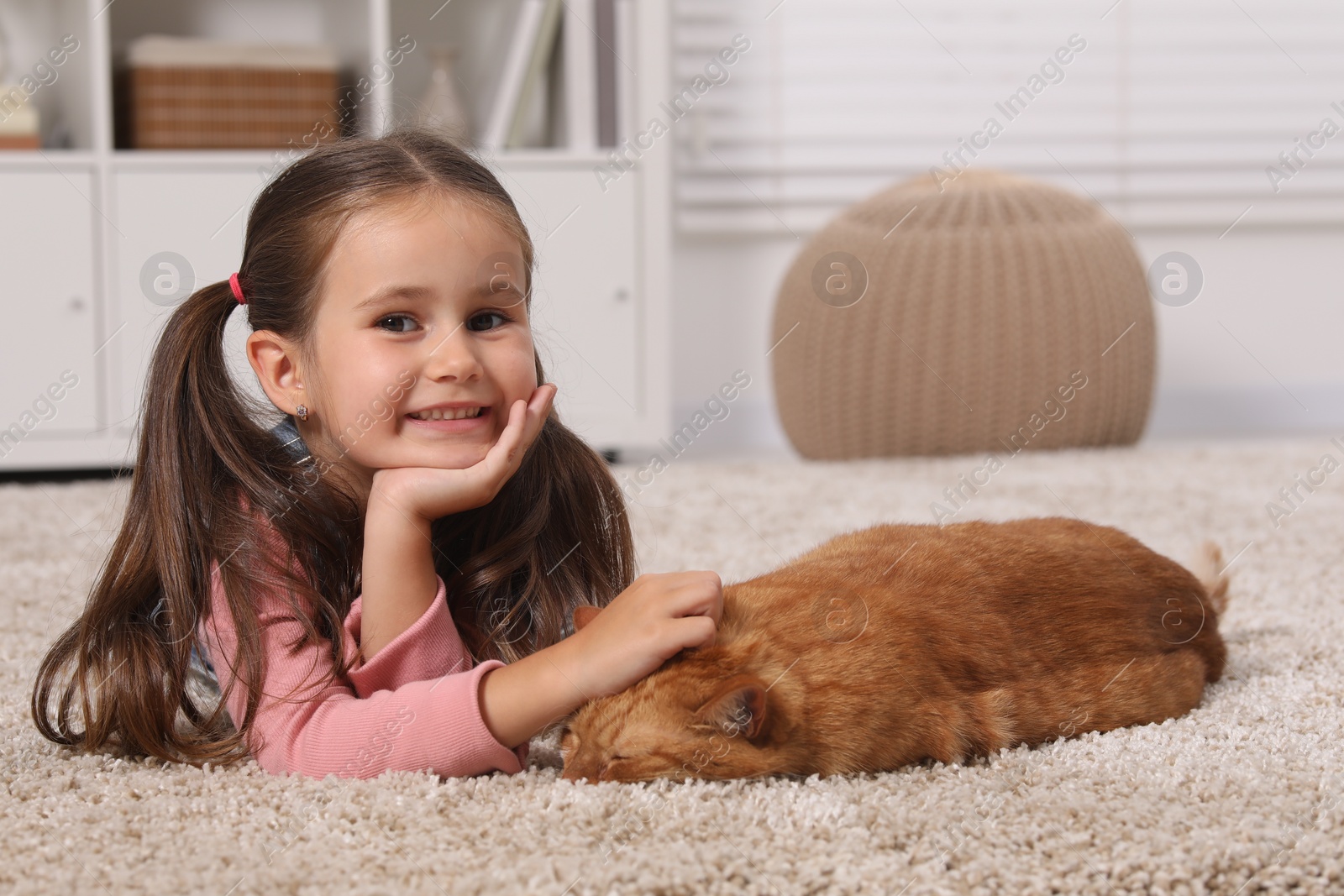 Photo of Happy little girl petting cute ginger cat on carpet at home