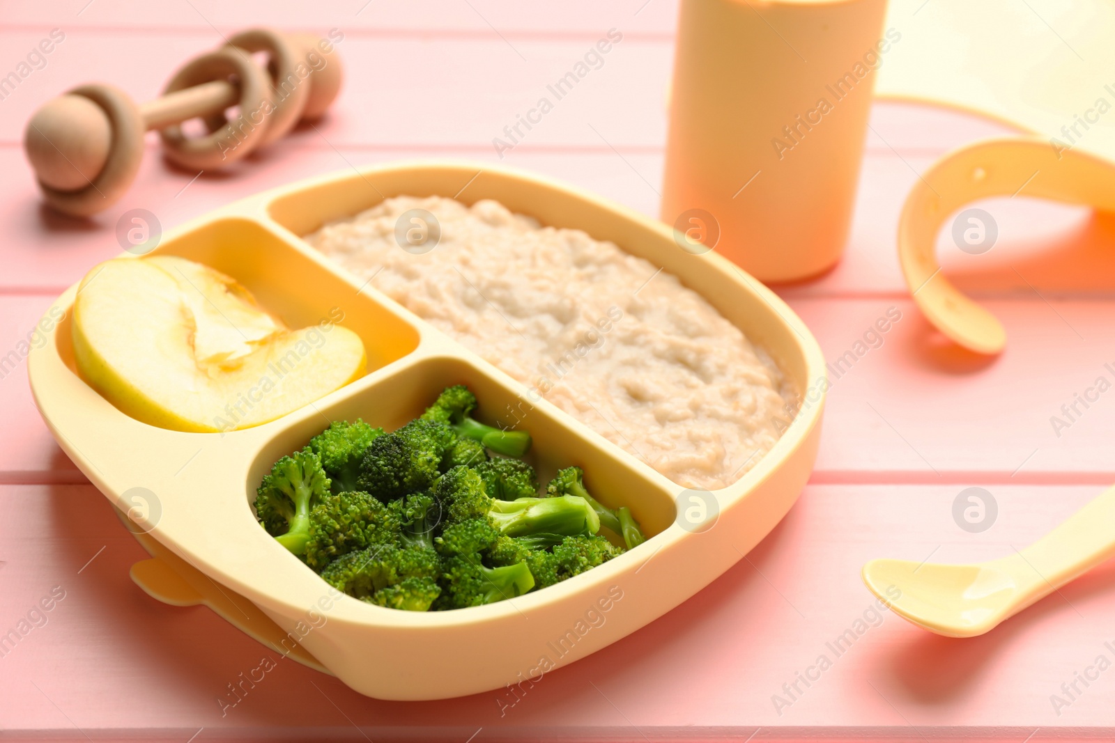 Photo of Plastic dishware with healthy baby food on pink wooden table, closeup