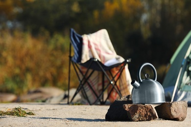 Photo of Metal kettle on rocks outdoors, space for text. Camping equipment
