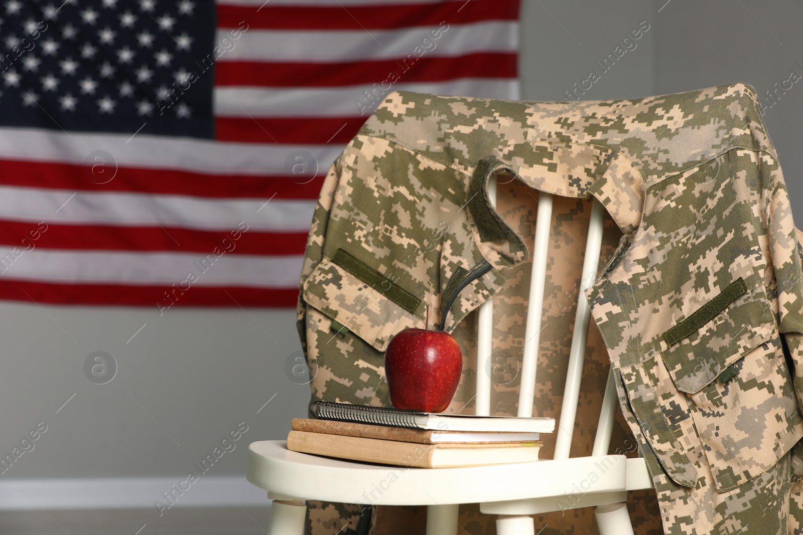 Photo of Chair with soldier uniform, notebooks and apple near flag of United States indoors, space for text. Military education