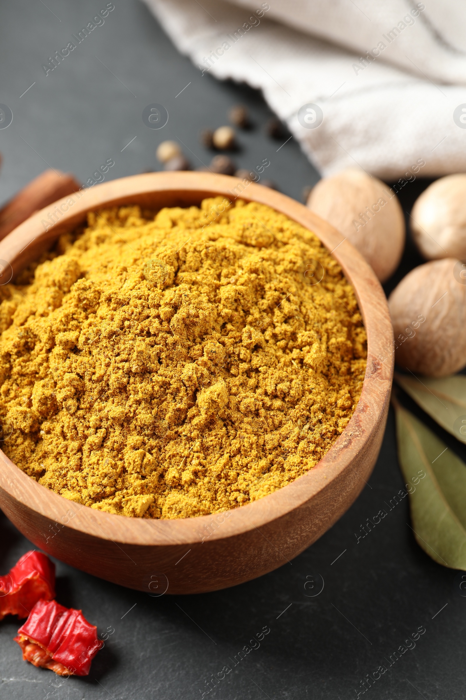 Photo of Dry curry powder in bowl and other spices on dark table, closeup