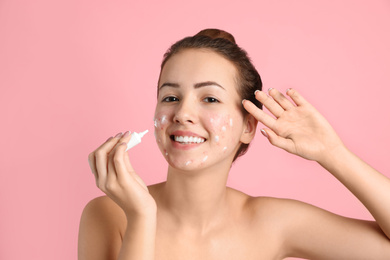 Photo of Teen girl with acne problem applying cream on light pink background