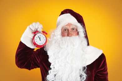 Photo of Santa Claus holding alarm clock on yellow background. Christmas countdown