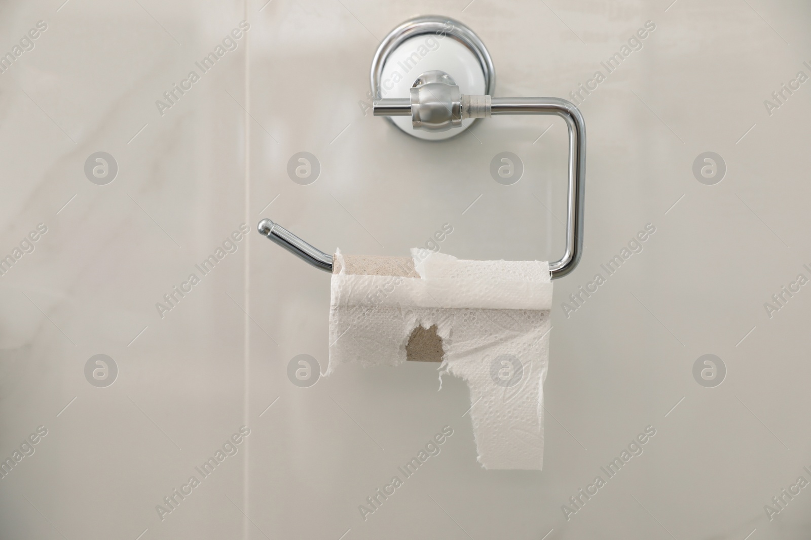 Photo of Holder with empty toilet paper roll on light wall indoors
