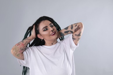 Photo of Beautiful young woman with tattoos on arms, nose piercing and dreadlocks against grey background