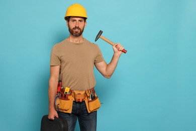 Photo of Professional builder in hard hat with hammer and tool belt on light blue background, space for text