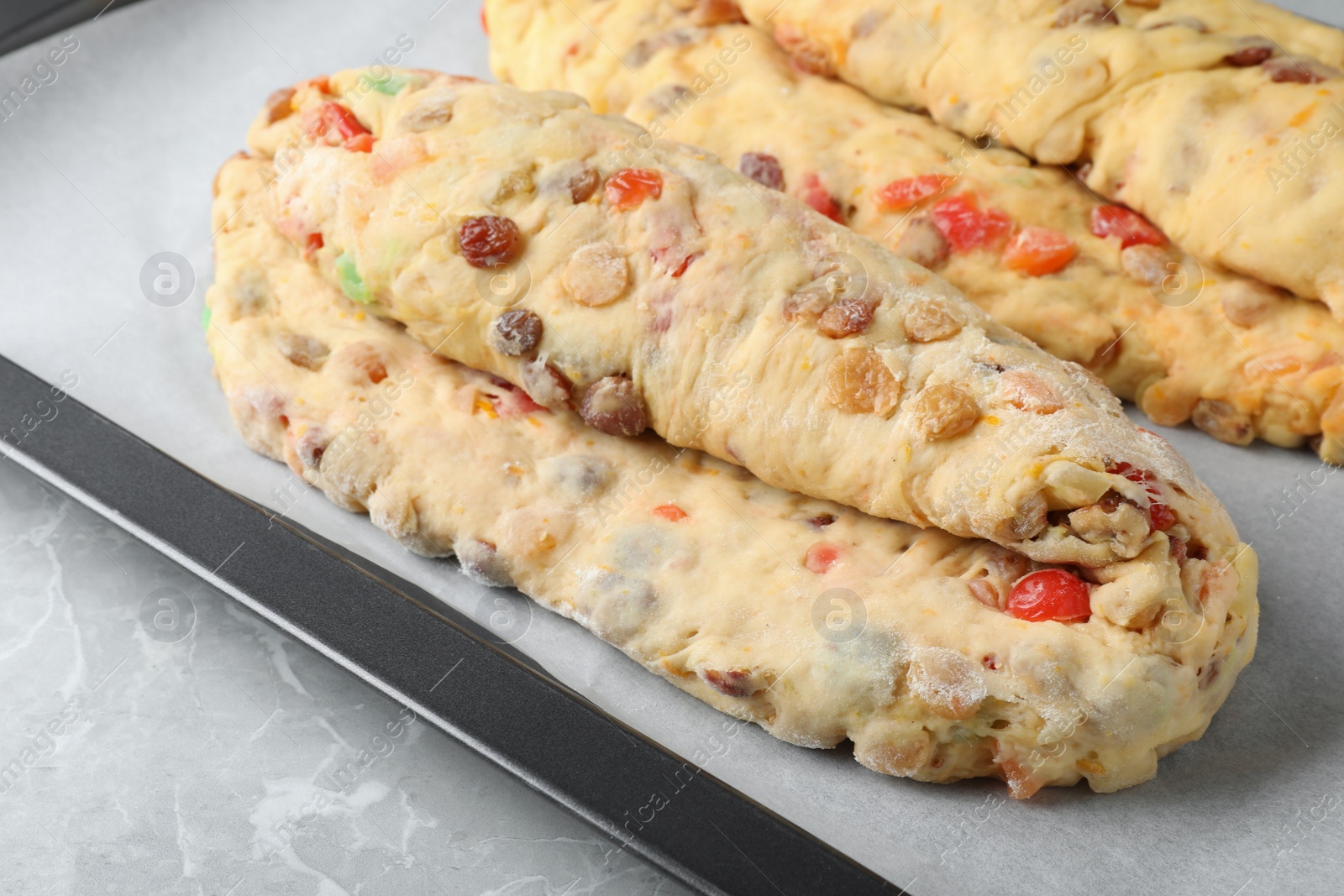 Photo of Baking tray with raw homemade Stollens on grey marble table, closeup. Traditional German Christmas bread