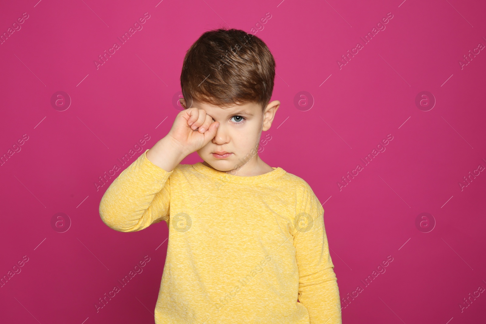 Photo of Little boy rubbing eye on color background. Annoying itch