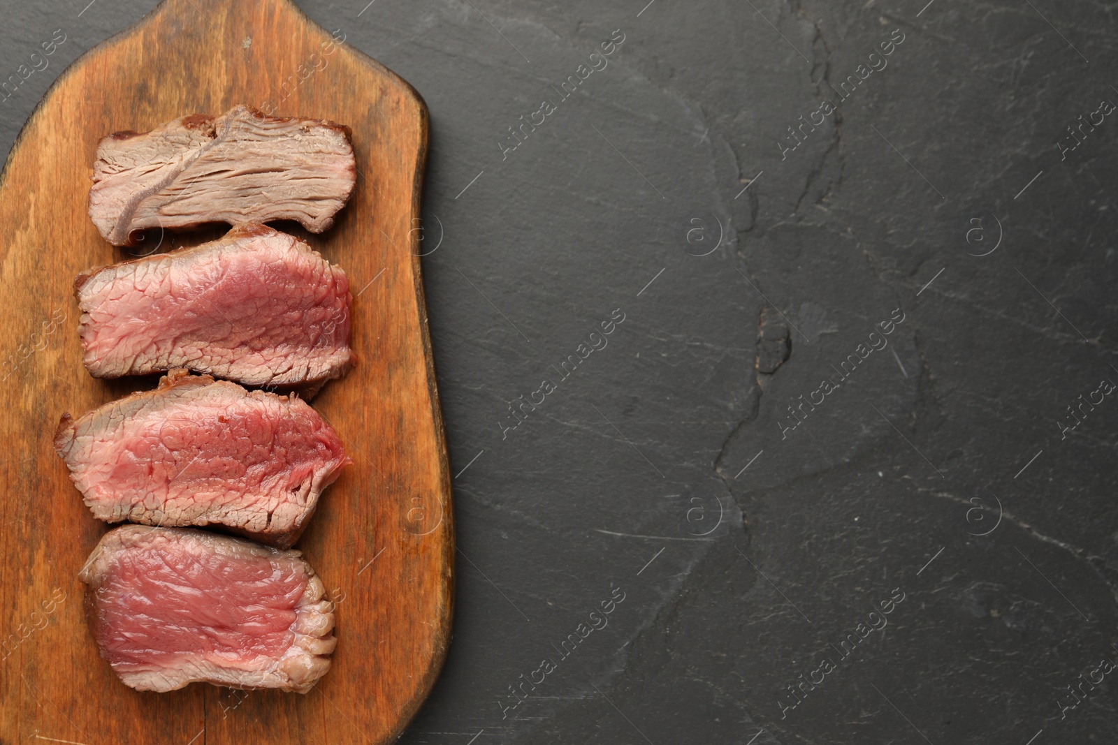 Photo of Delicious sliced beef tenderloin with different degrees of doneness on black table, top view. Space for text