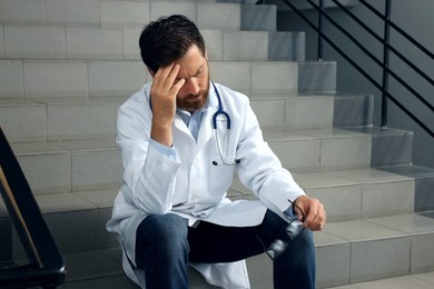 Photo of Tired doctor sitting on stairs in hospital