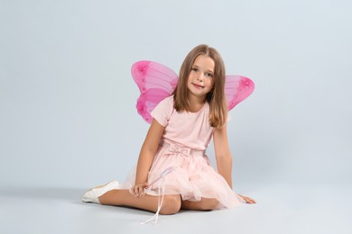 Photo of Cute little girl in fairy costume with pink wings and magic wand on light background