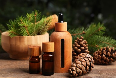 Photo of Bottlespine essential oil, conifer tree branches and cones on wooden table