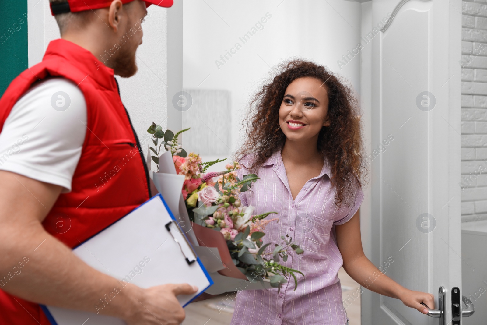 Photo of African-American woman receiving flower bouquet from delivery man indoors