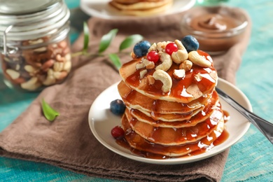 Stack of tasty pancakes with berries, nuts and syrup on table