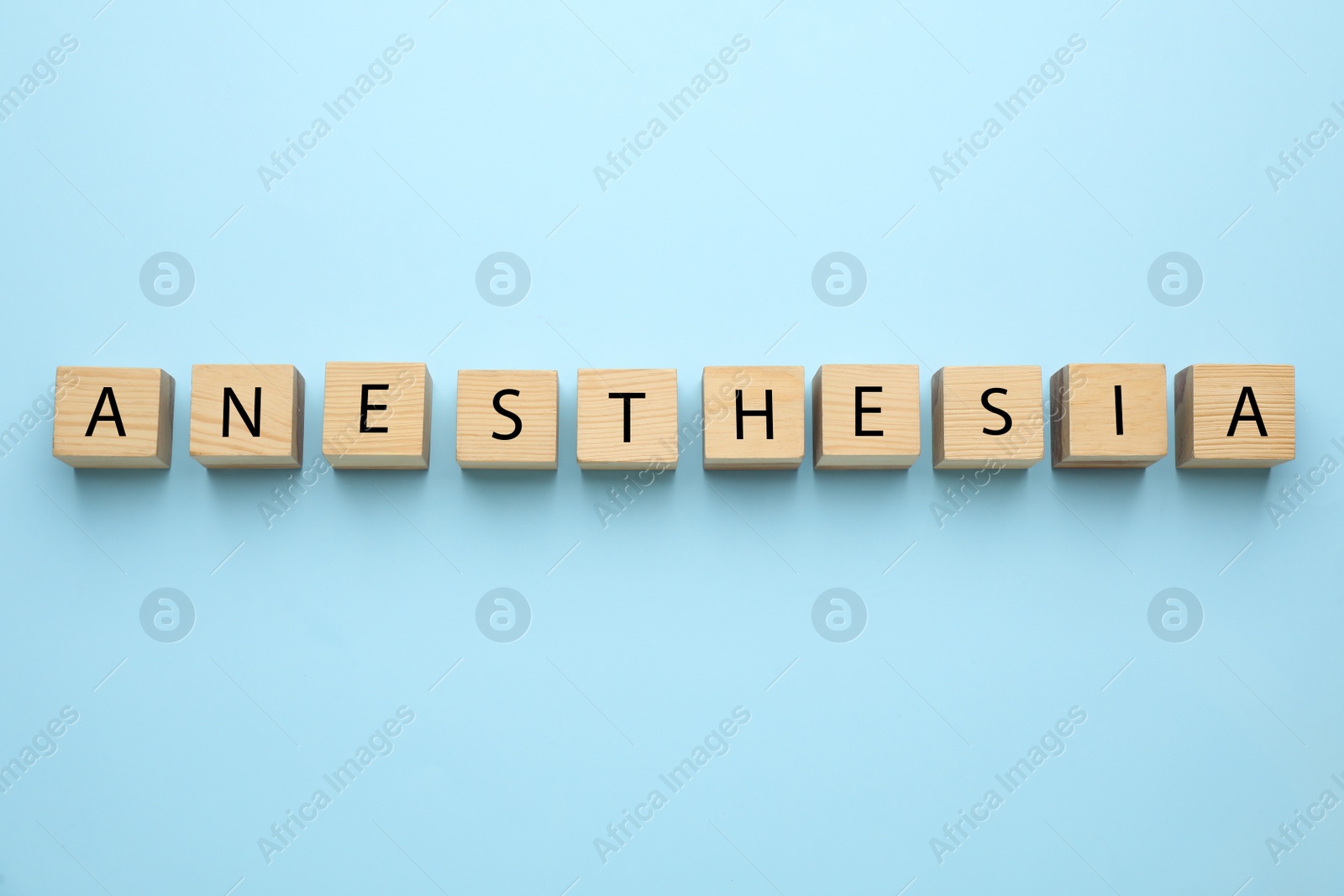 Photo of Wooden cubes with word Anesthesia on light blue background, top view