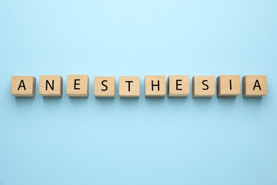 Photo of Wooden cubes with word Anesthesia on light blue background, top view
