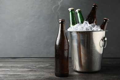 Photo of Metal bucket with bottles of beer and ice cubes on black wooden table. Space for text