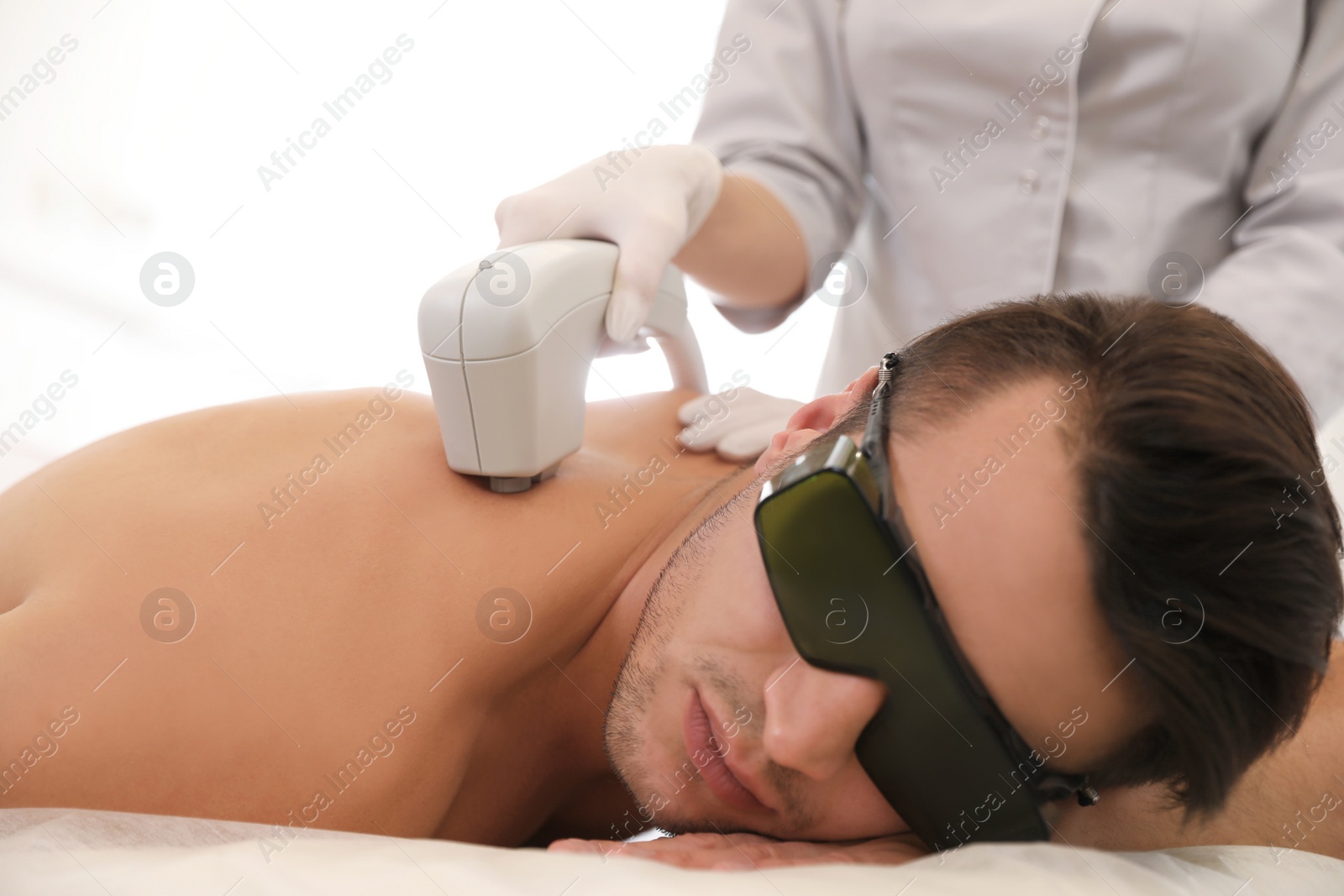 Photo of Young man undergoing laser epilation procedure in beauty salon