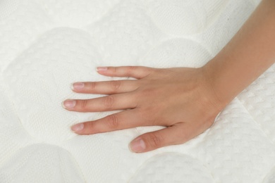 Photo of Young woman touching modern orthopedic mattress, closeup